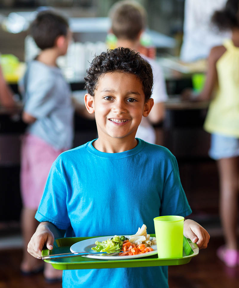Portrait,Of,Happy,Schoolboy,Holding,Food,Tray,In,Canteen,Against